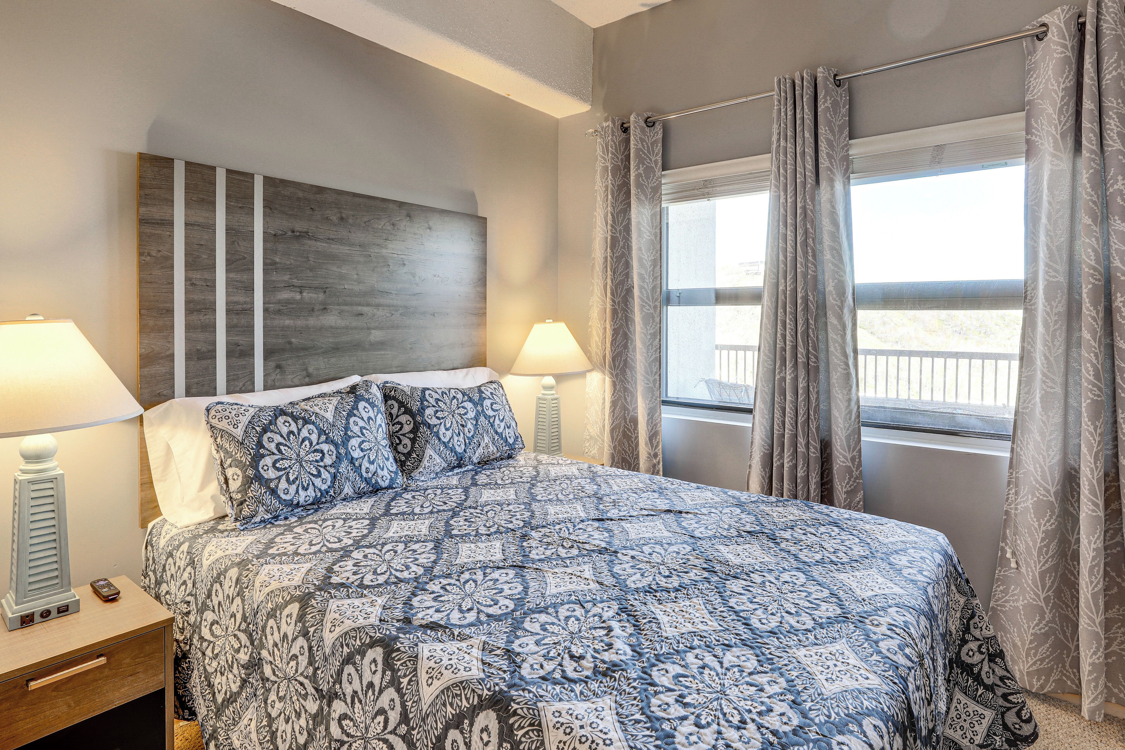 A bedroom with a bed, two bedside tables, a nightstand, a window with curtains, and a view of the outside.