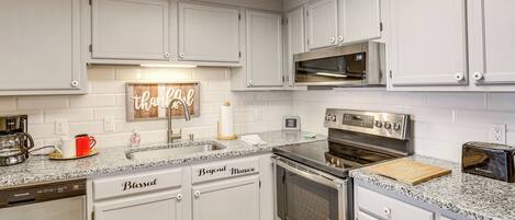 A modern kitchen with white cabinets, a granite countertop, a dishwasher, a stove, and a toaster.