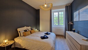 Et soveværelse med seng, sengebord, lampe, kommode og et vindue med gardiner.