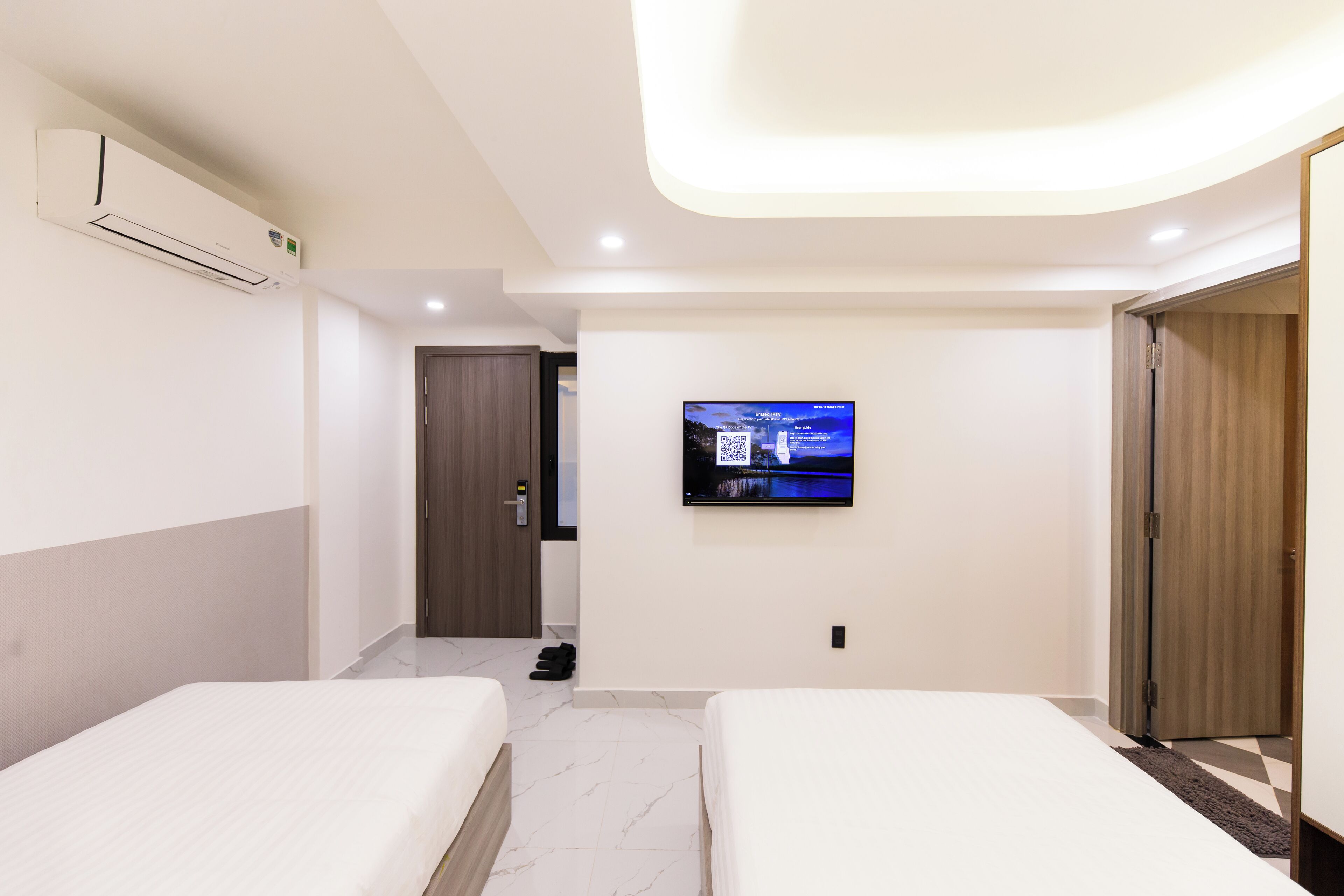Una habitación de hotel moderna con dos camas, un televisor montado en la pared y un equipo de aire acondicionado.