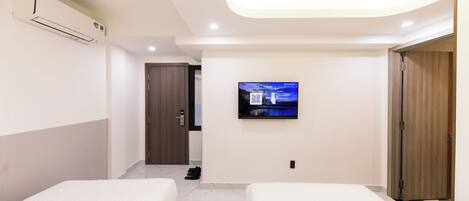 Una habitación de hotel moderna con dos camas, un televisor montado en la pared y un equipo de aire acondicionado.