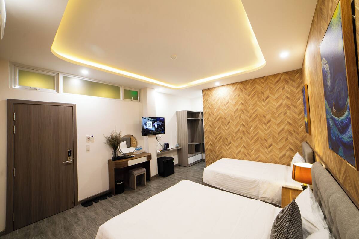 A hotel room with two beds, a desk with a computer, a TV, and a herringbone-patterned wall.