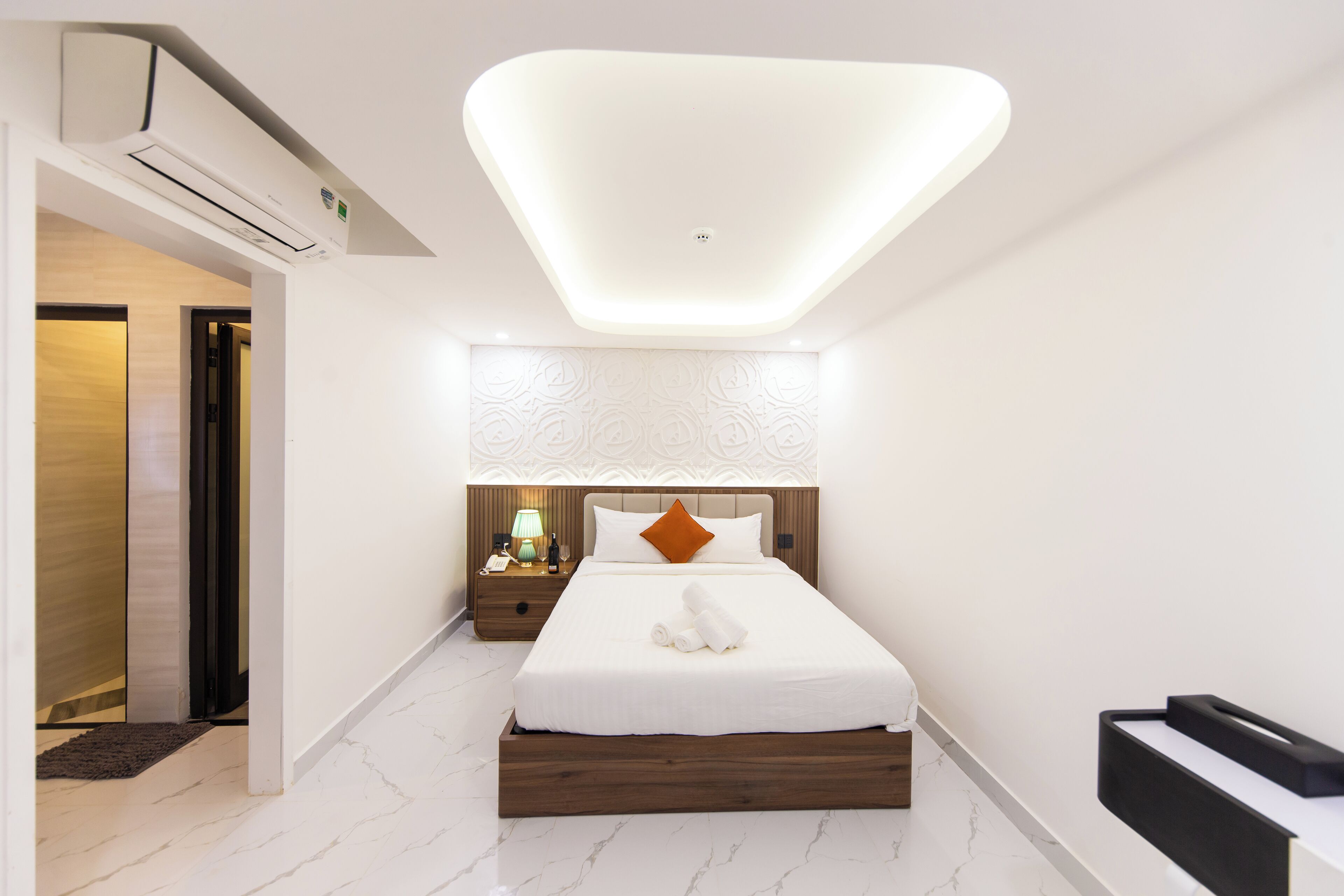 Une chambre d’hôtel moderne avec un lit soigneusement fait, une table de chevet avec une lampe et un système de climatisation intégré.