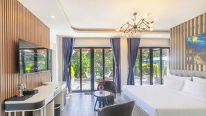 A modern hotel room with a large bed, a desk with a flat-screen TV, a chair, and a small table with a vase. - TP Dalat Hotel (Xuan Huong - Da Lat)