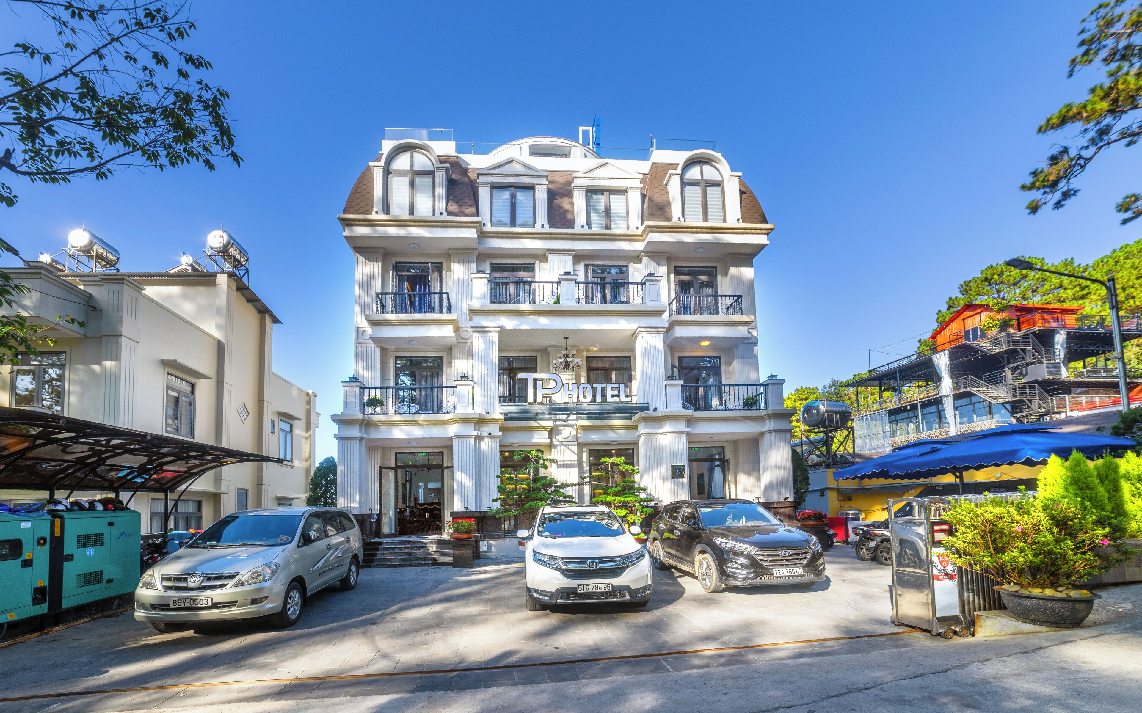 A hotel with a classic architectural style, featuring a central entrance, multiple balconies, and a parking area with several cars.