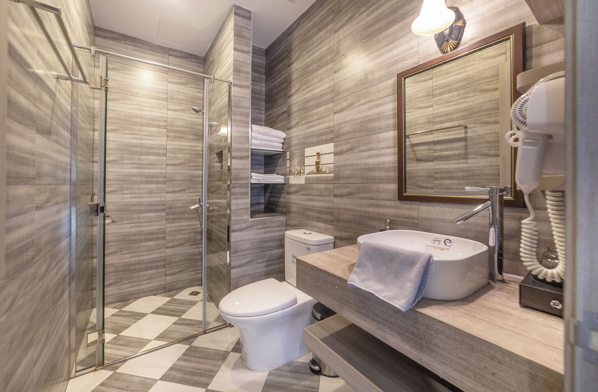 A modern bathroom with a glass shower enclosure, a toilet, a sink with a towel, and a mirror with a clock.