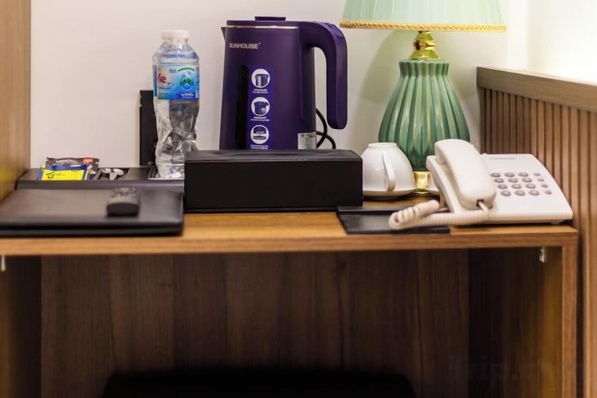 A wooden desk with a black electronic device, a white telephone, a water bottle, and a purple coffee maker.