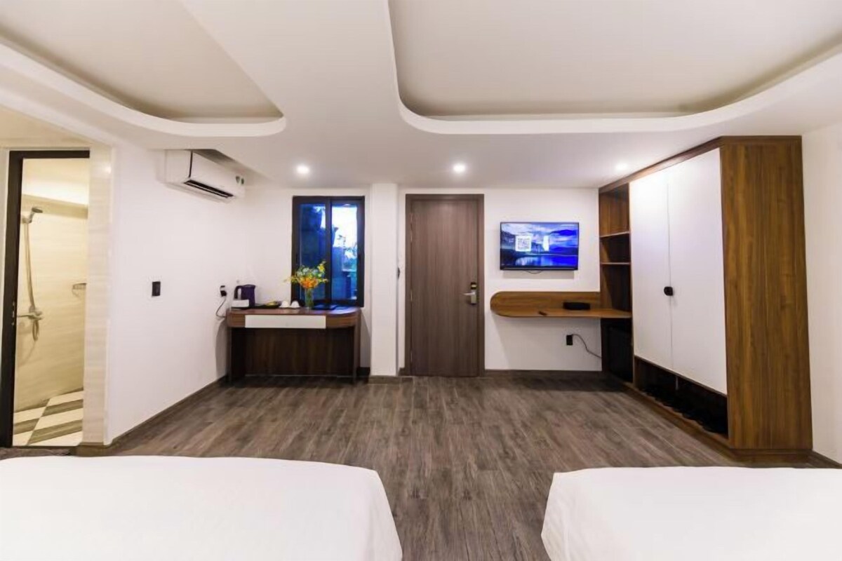 A hotel room with two beds, a TV, a desk with a sink, and a wardrobe.