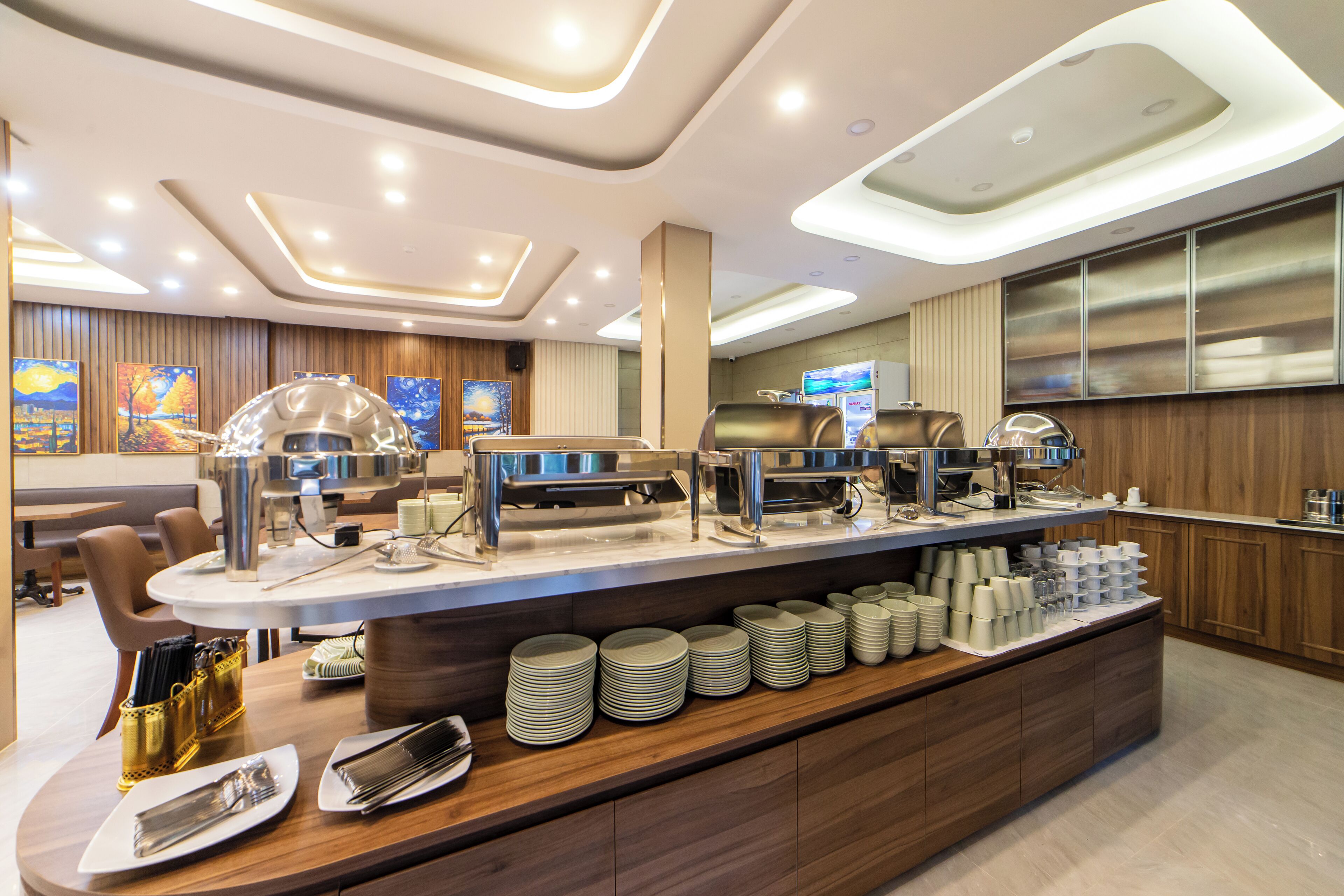 A modern hotel buffet with a central serving counter, multiple food stations, and a seating area with tables and chairs.