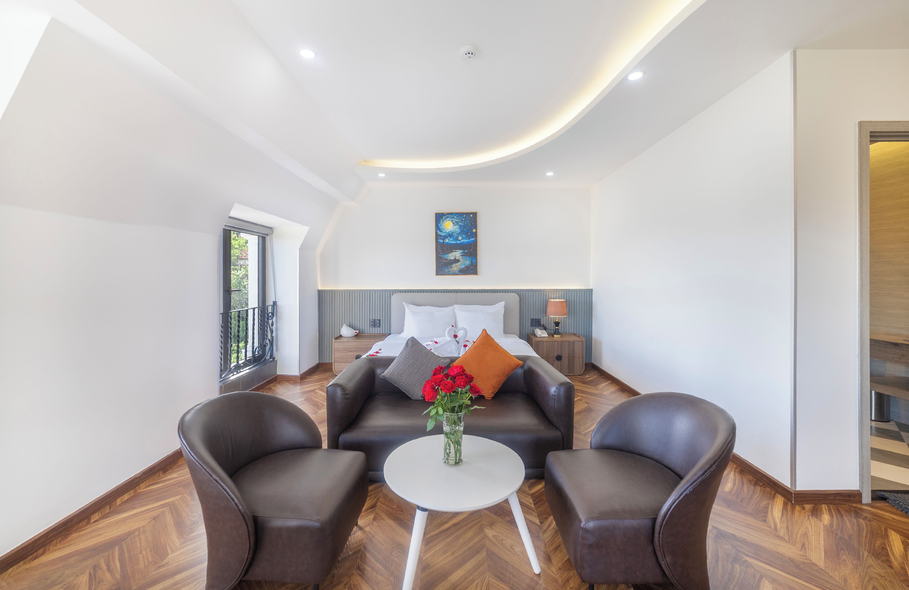 A modern hotel room with a bed, two leather armchairs, a small table, and a painting on the wall.
