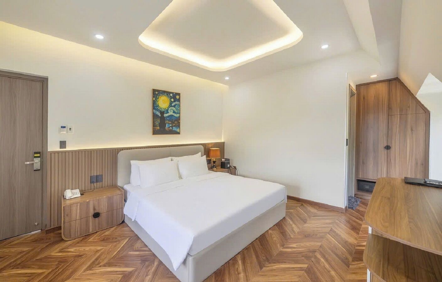 A modern hotel room with a large bed, wooden flooring, a painting on the wall, and a wooden wardrobe.