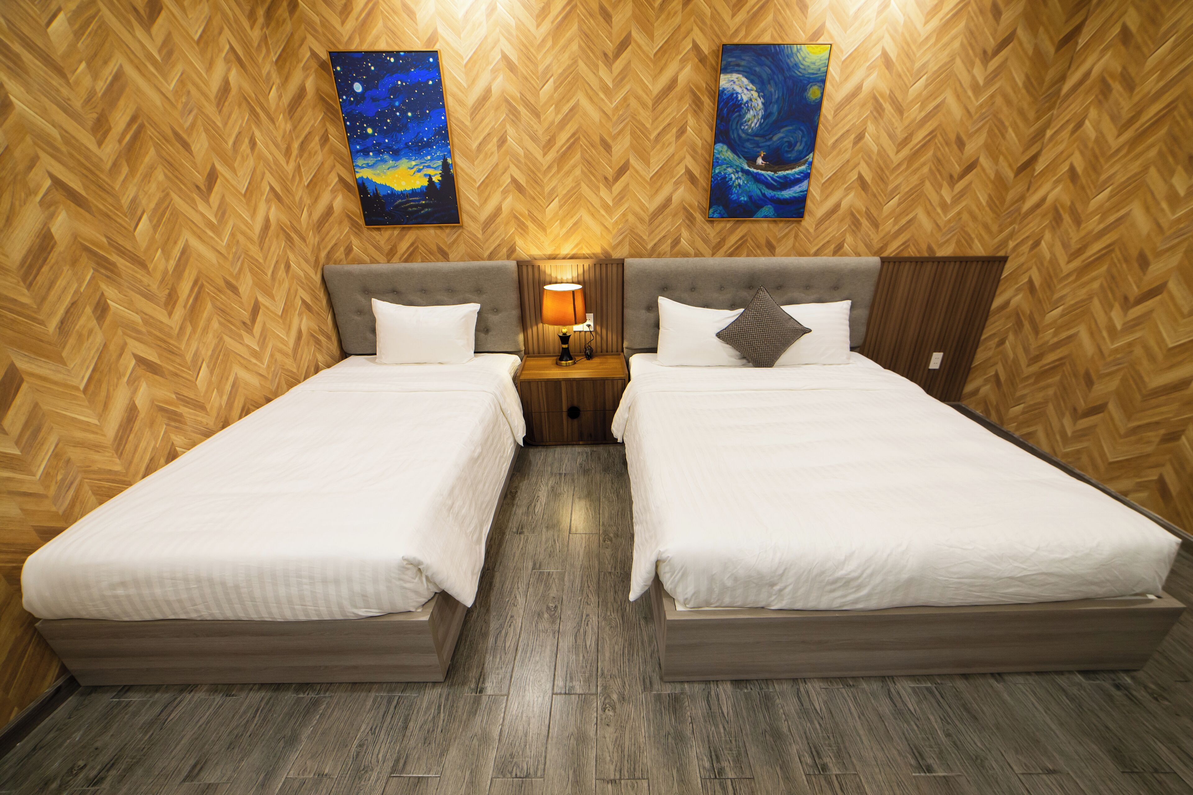 A hotel room with two beds, wooden herringbone-patterned walls, and two paintings.