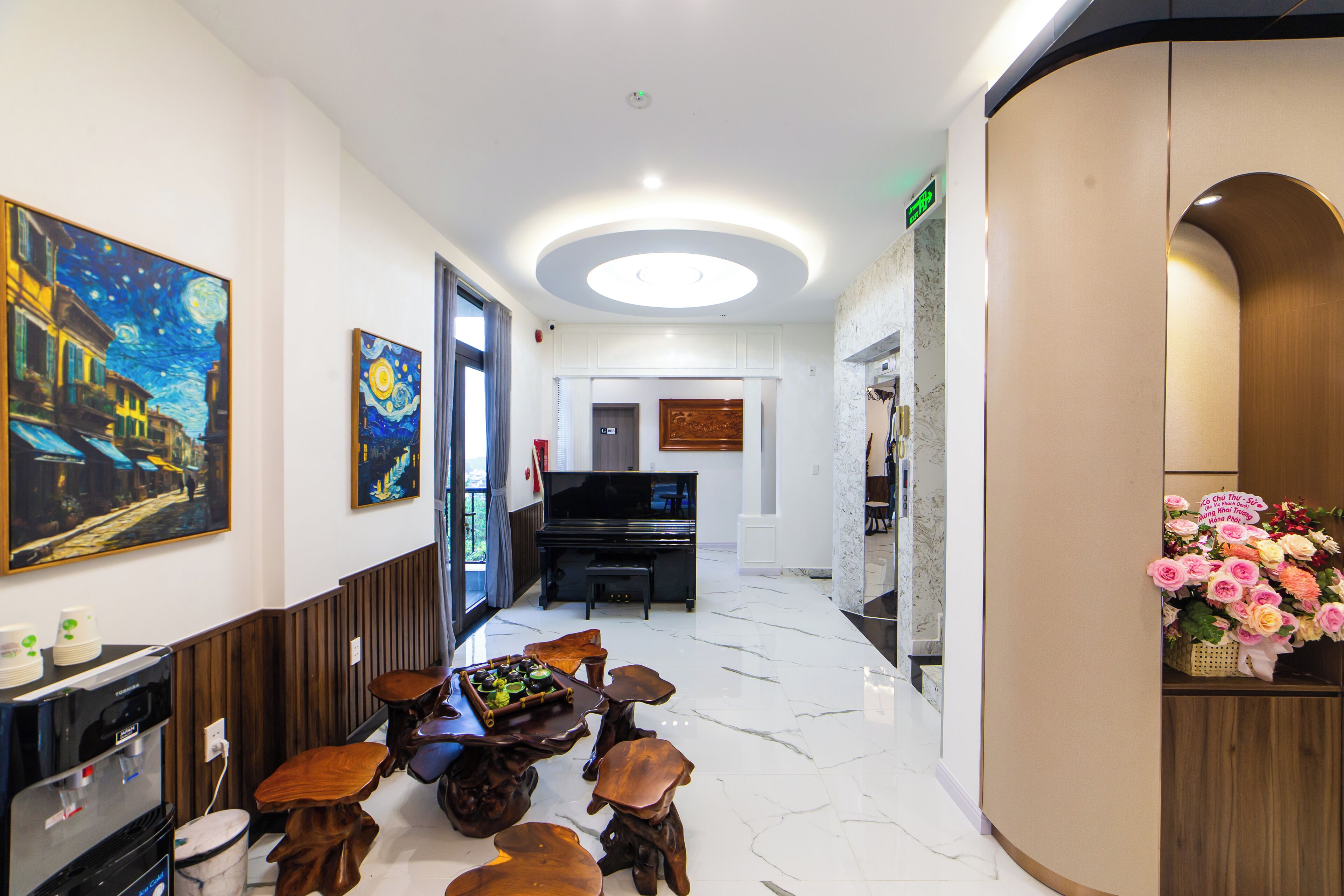 A modern hotel lobby with a piano, a dining area with wooden stools, and a floral arrangement.