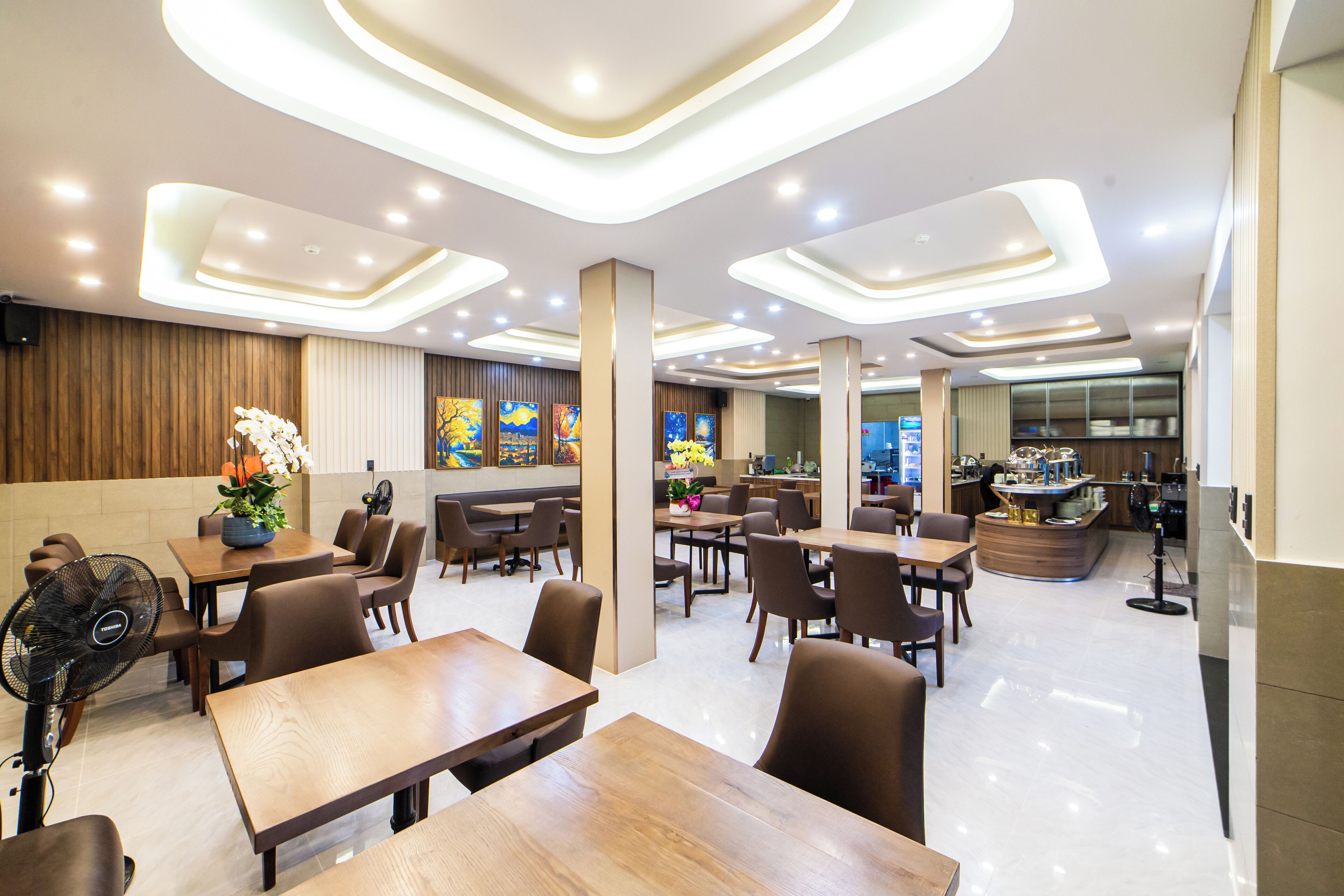 A modern restaurant with wooden tables and chairs, a fan, and a counter with a menu.