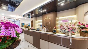 A hotel reception area with a modern design, featuring a reception desk, a sign with the hotel name, and decorative flowers. - TP Dalat Hotel (Xuan Huong - Da Lat)