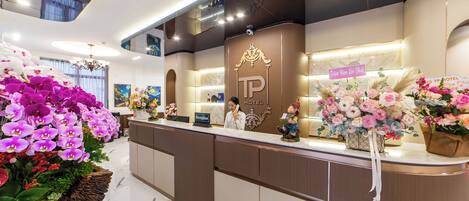A hotel reception area with a modern design, featuring a reception desk, a sign with the hotel name, and decorative flowers.