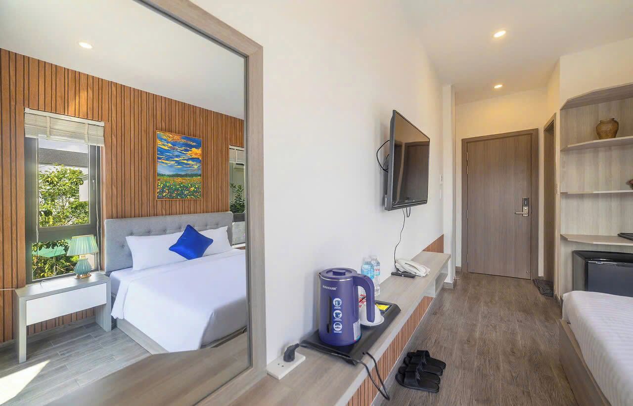 A modern hotel room with a bed, a coffee maker, a TV, and a mirror.