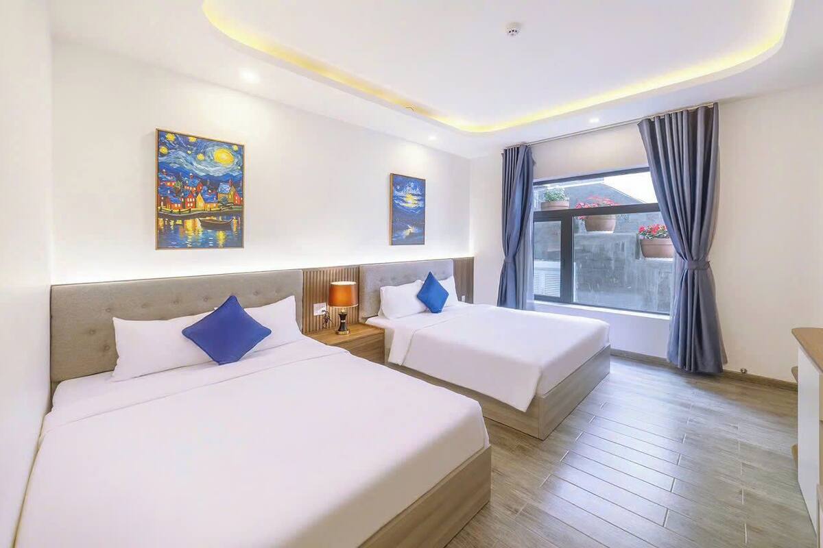 A hotel room with two beds, a nightstand, a lamp, and artwork on the walls.