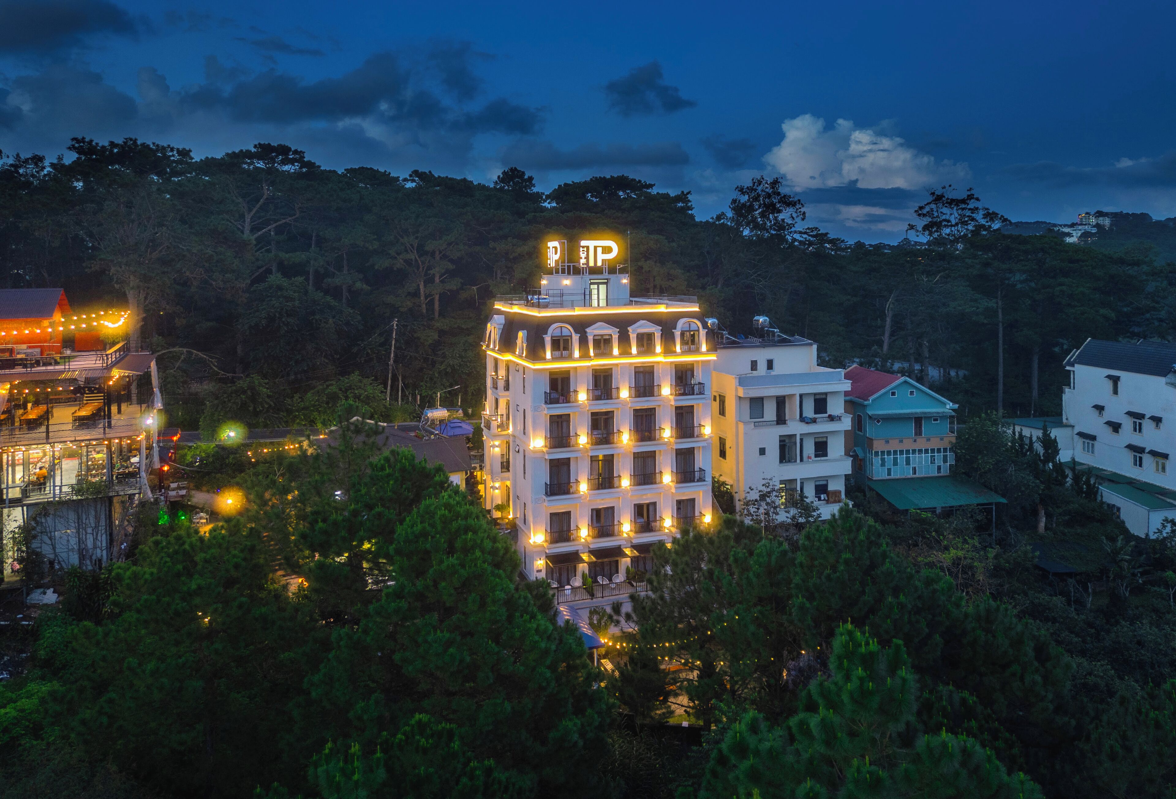 Ein mehrstöckiges Hotel mit beleuchteter Beschilderung und Balkonen, umgeben von Bäumen und anderen Gebäuden.
