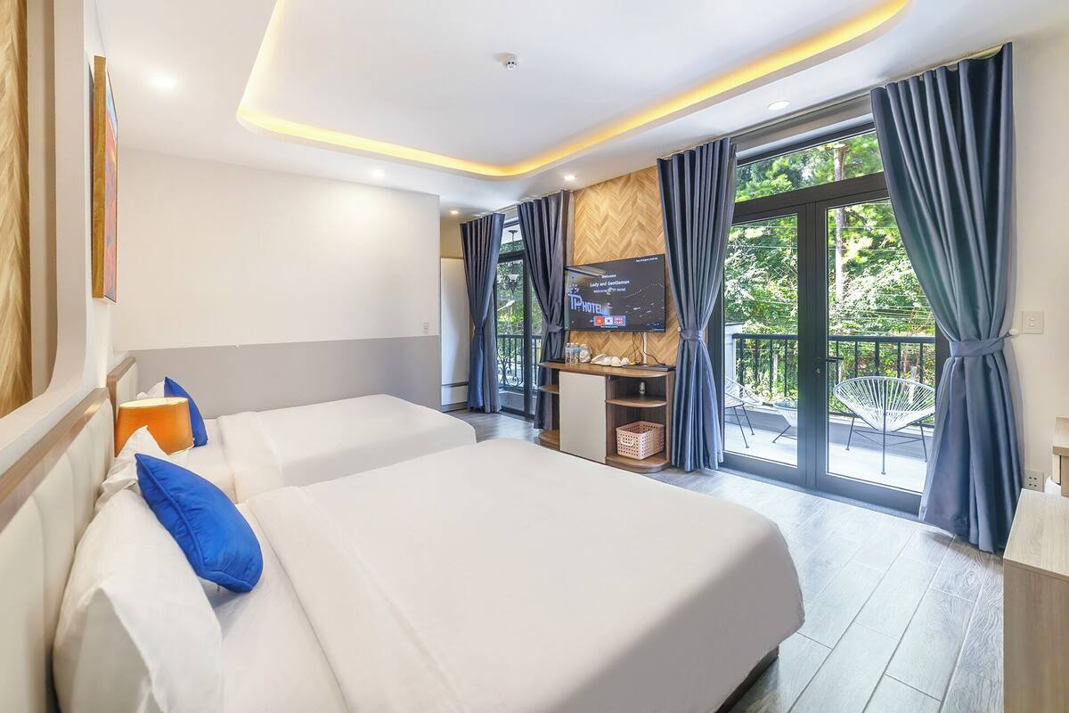 A hotel room with two beds, a TV, and a balcony with curtains.