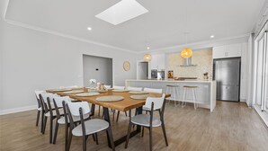 Une cuisine moderne avec des meubles blancs, un réfrigérateur en acier inoxydable et un coin repas comprenant une table en bois et des chaises blanches.
