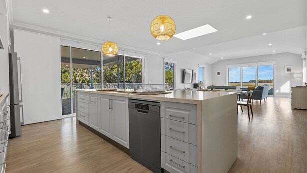 Une cuisine moderne dotée d’un grand îlot central, d’un lave-vaisselle intégré et de luminaires suspendus.