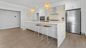 Une cuisine moderne dotée d’un îlot central, d’appareils électroménagers en acier inoxydable et de luminaires suspendus.