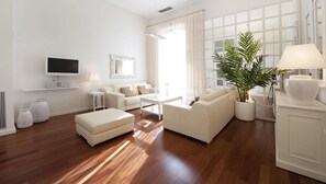 Uma sala de estar moderna com televisão de tela plana, sofás brancos, uma mesa de centro e uma grande planta em vaso.