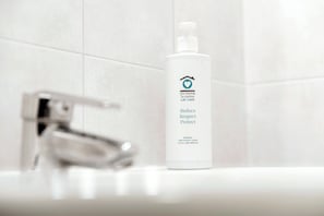 Un baño con lavamanos blanco, grifo cromado y una botella de jabón orgánico para cabello y cuerpo.