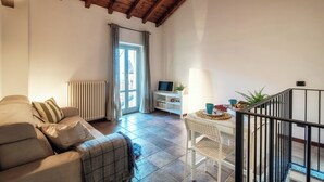 A living room with a sofa, a TV stand, a dining table with chairs, and a staircase. - Lake Nest (Carate Urio)