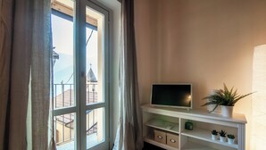 A room with a large window, a flat-screen TV on a white console, and a potted plant. - Lake Nest (Carate Urio)