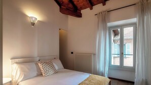 A bedroom with a bed, a bedside table, a wall-mounted light, a window with curtains, and a radiator. - Lake Nest (Carate Urio)