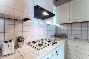 Una cocina con gabinetes blancos, una estufa a gas, un tostador y una planta en maceta.