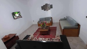 A living room with a black sofa, a wooden coffee table, a red rug, and a ceiling fan. - Super Appartement S+2 Spacieux au Cœur de Bizerte (Bizerte)