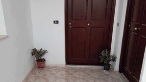 A hallway with a marble floor, a wooden door, and two potted plants. - Super Appartement S+2 Spacieux au Cœur de Bizerte (Bizerte)