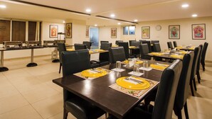 Un salón de conferencias con varias mesas dispuestas para comer, equipado con sillas y cubiertos.