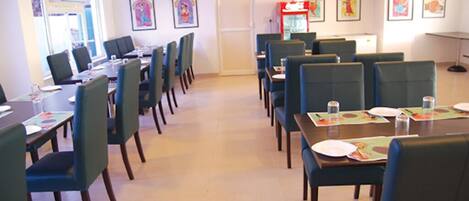 A dining area with multiple tables and chairs, framed artwork on the walls, and a vending machine in the background.