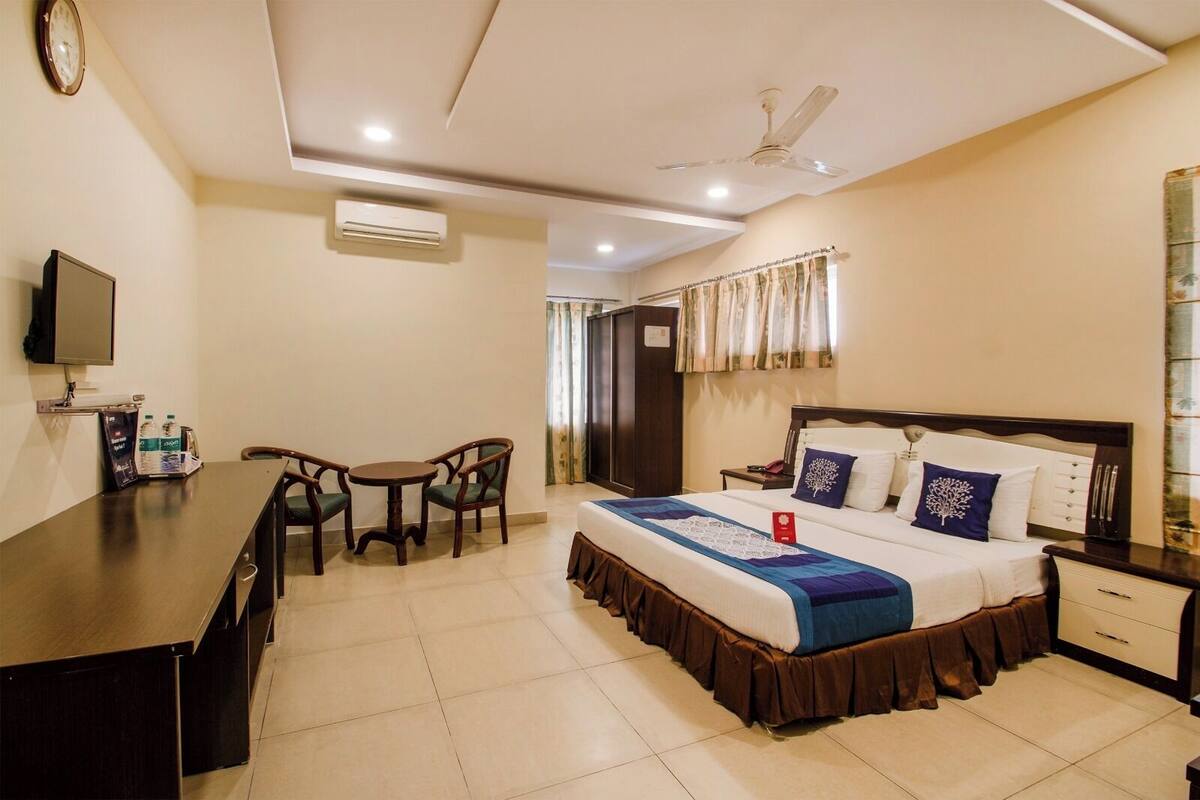 A hotel room with a bed, bedside table, nightstand, desk, chairs, and a television.