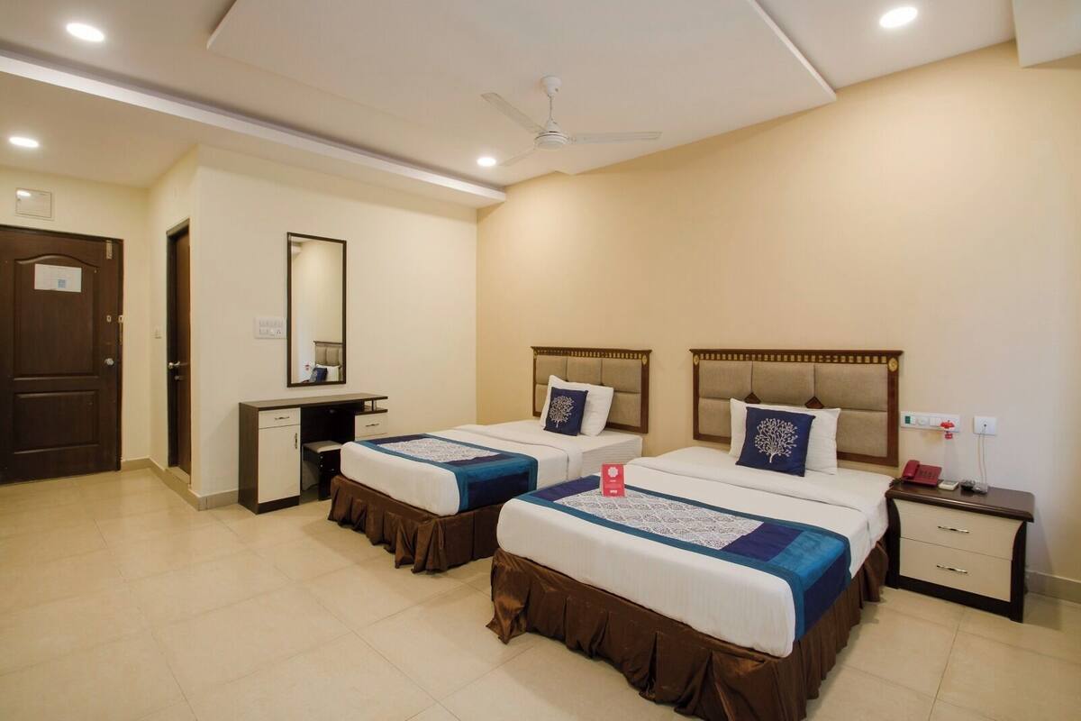 A hotel room with two beds, a desk, a mirror, a nightstand, and a ceiling fan.