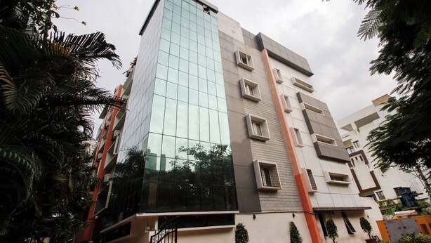Un edificio moderno de varios pisos con fachada de vidrio, varios balcones y una entrada protegida por una reja.