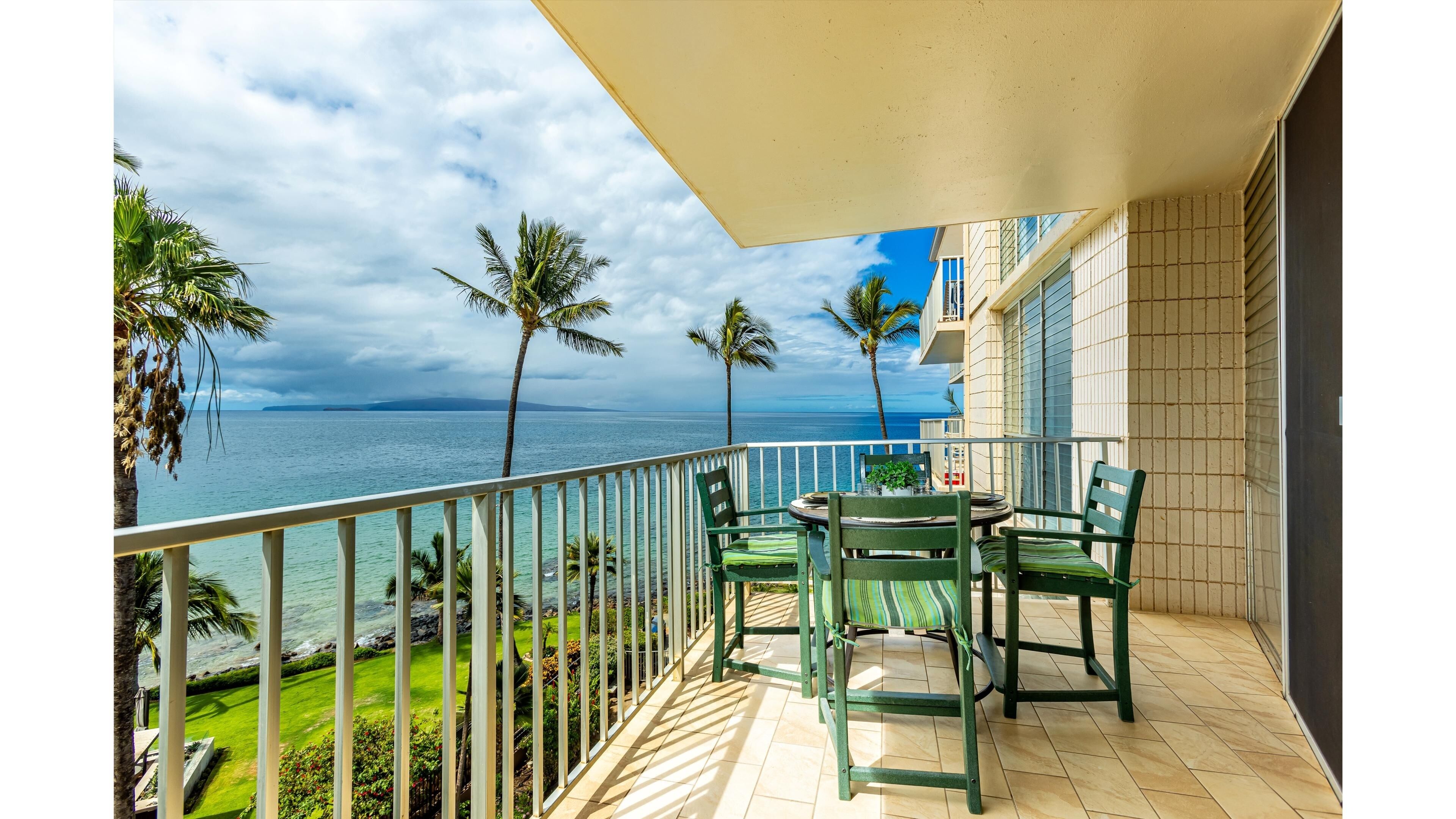 A balcony with a view of the ocean, two chairs, and a table.