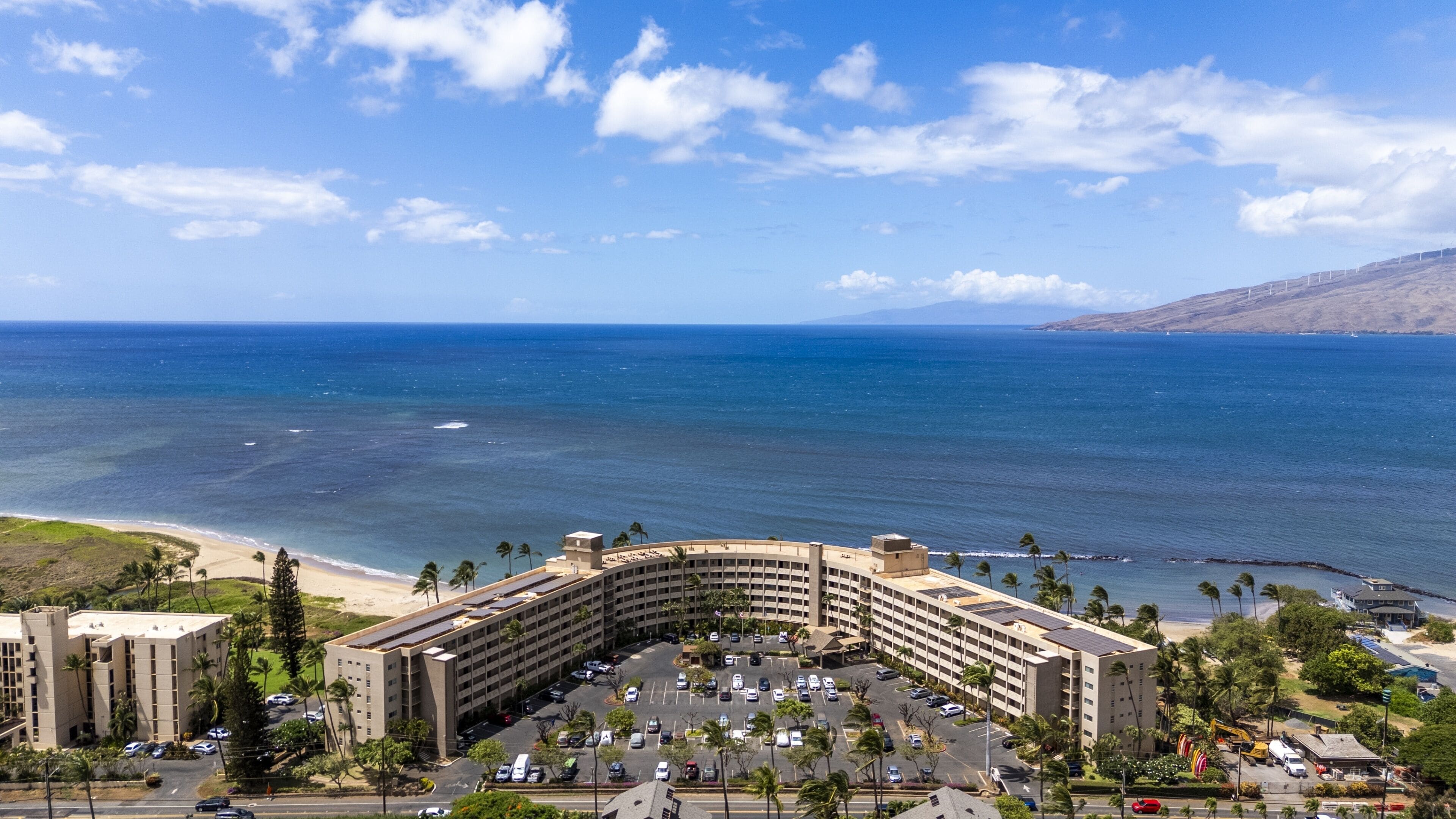 Ein Hotel mit geschwungener Architektur, einem Parkplatz und Blick aufs Meer.