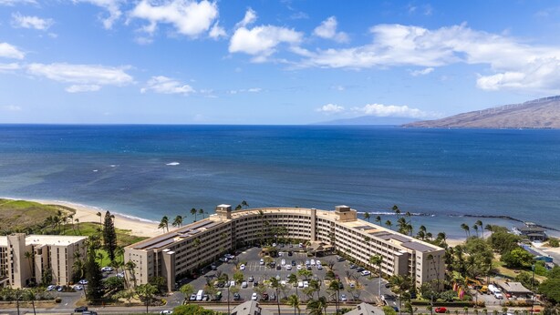 Ein Hotel mit geschwungener Architektur, einem Parkplatz und Blick aufs Meer.