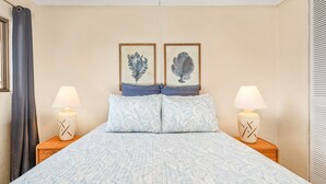 Ein Bett mit gesteppter Bettdecke, zwei Kissen, zwei Nachttische mit Lampen und zwei gerahmte Bilder an der Wand.