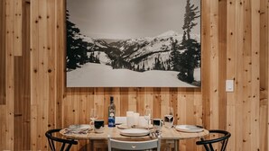 Ein Esstisch ist gedeckt mit Tellern, Gläsern und einer Flasche, vor einer Holzwand mit einem großen Schwarz-Weiß-Landschaftsbild von Bergen.
