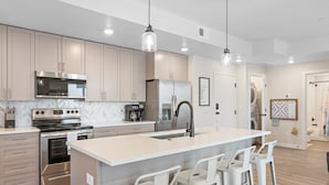 A modern kitchen with stainless steel appliances, a large island with bar stools, and pendant lighting. - Paddle Away 2 Bedroom Condo (St. George)