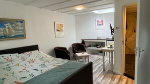 A bedroom with a bed, a desk, a chair, and a computer. There is a painting on the wall and a door leading to a bathroom. - Renovated studio, near the forest and center (Bergen)