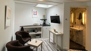 A compact living space with a kitchenette, a flat-screen TV, a seating area with a coffee table, and a bathroom with a marble sink. - Renovated studio, near the forest and center (Bergen)