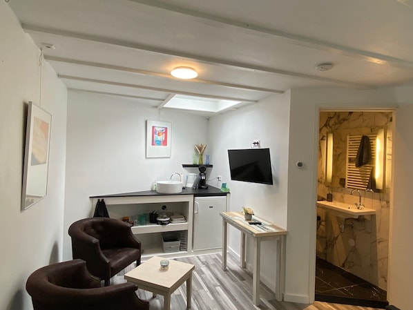 Un espace de vie compact comprenant une kitchenette, un téléviseur à écran plat, un coin salon avec une table basse et une salle de bain dotée d’un lavabo en marbre.