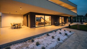 Una casa moderna con un porche cubierto, mobiliario de exterior y una escalera visible que conduce al interior.
